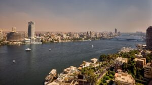 Aerial view of the cityscape, with Sheraton Cairo Hotel, riverboats, and buildings under a clear sky.