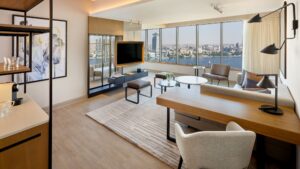 Modern Sheraton Cairo living room with city view, sofa, table, TV, and large windows.