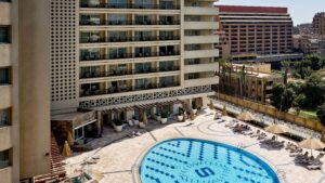 Aerial view of Sheraton Cairo Hotels pool with lounge chairs by a tall building.