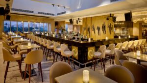 Sheraton Cairos bar: beige chairs, central counter, city view through large windows.