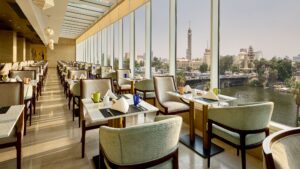 Spacious restaurant at Sheraton Cairo with large windows overlooking the cityscape and river.