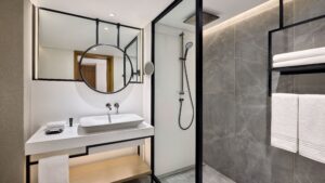 Modern bathroom at Sheraton Cairo Hotel with round mirror, sink, and walk-in shower.