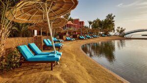 Beach at Sheraton Miramar with straw umbrellas, blue chairs, and calm water under a clear sky.