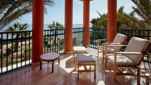 Sunny beach view from Sheraton Miramar Resorts outdoor patio with chairs, table, and palm trees.
