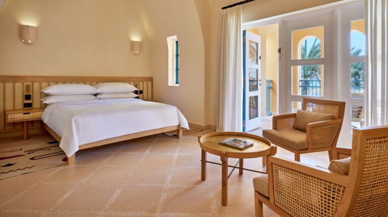 Sheraton Miramar Resort room: bed, seating area, and balcony with palm trees view.