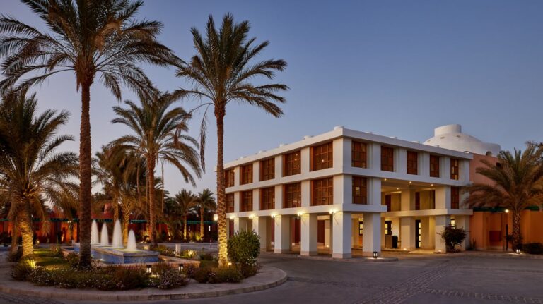 A modern two-story at Sheraton Miramar with palm trees and a fountain at sunset.