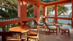 Terrace with wooden furniture, overlooking palm trees and water at Sheraton Miramar Resort.