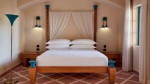 Modern Sheraton Miramar room with a wooden bed, white sheets, wall lights, and a canopy.