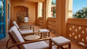 Sheraton Miramar Resort terrace with wooden chairs, table, and a hanging wicker chair with cushions.