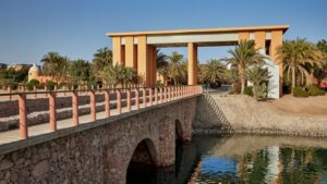 Stone bridge by the Sheraton Miramar leads to an archway, framed by palms under a clear sky.