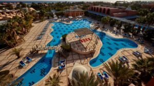 Large outdoor pool area at Sheraton Miramar Resort, lined with sun loungers and palm trees.