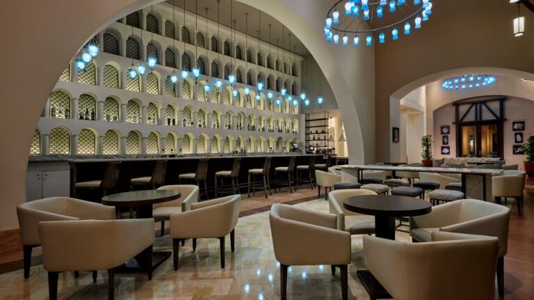 Elegant lounge at Sheraton Miramar Resort with a bar, neutral chairs, and blue pendant lights.