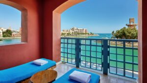 A balcony at Sheraton Miramar Resort overlooks a turquoise sea and distant buildings.