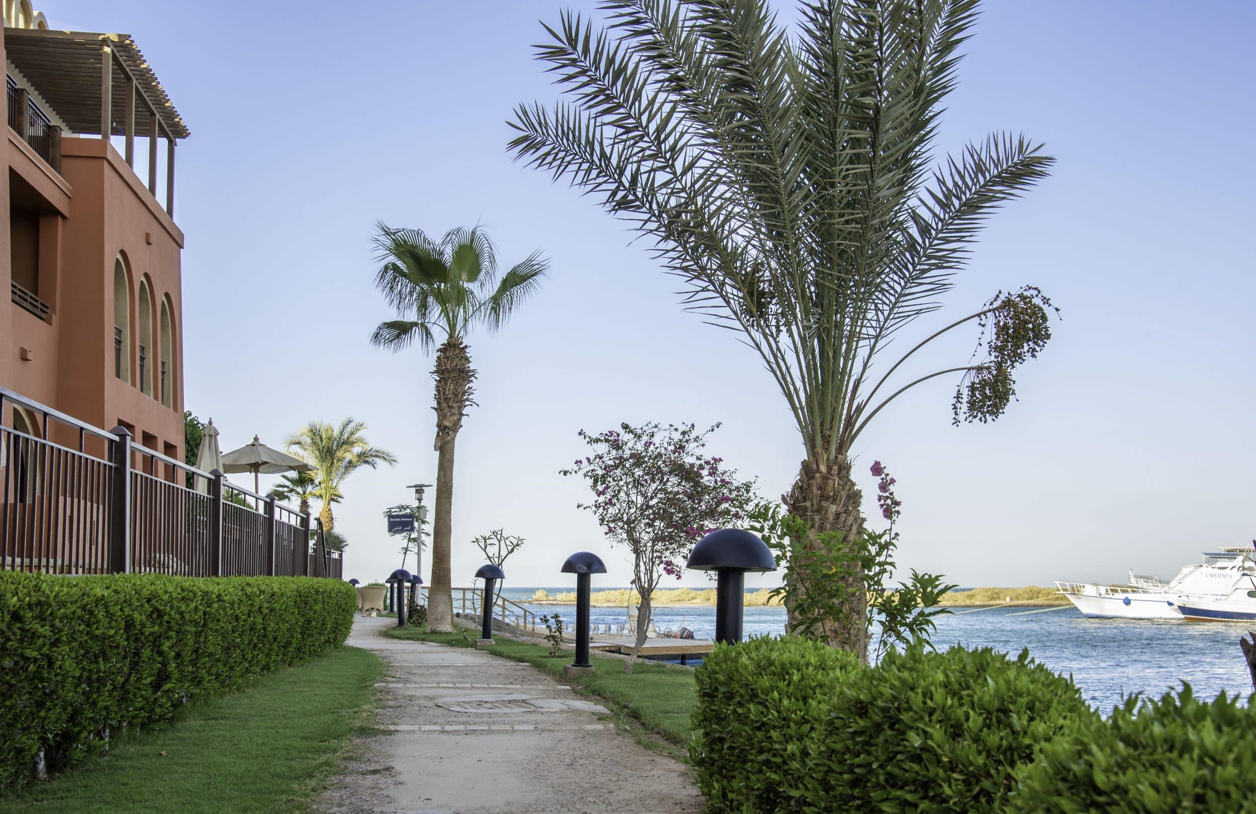 A riverside path by the Three Corners Ocean View with palm trees and a docked yacht.