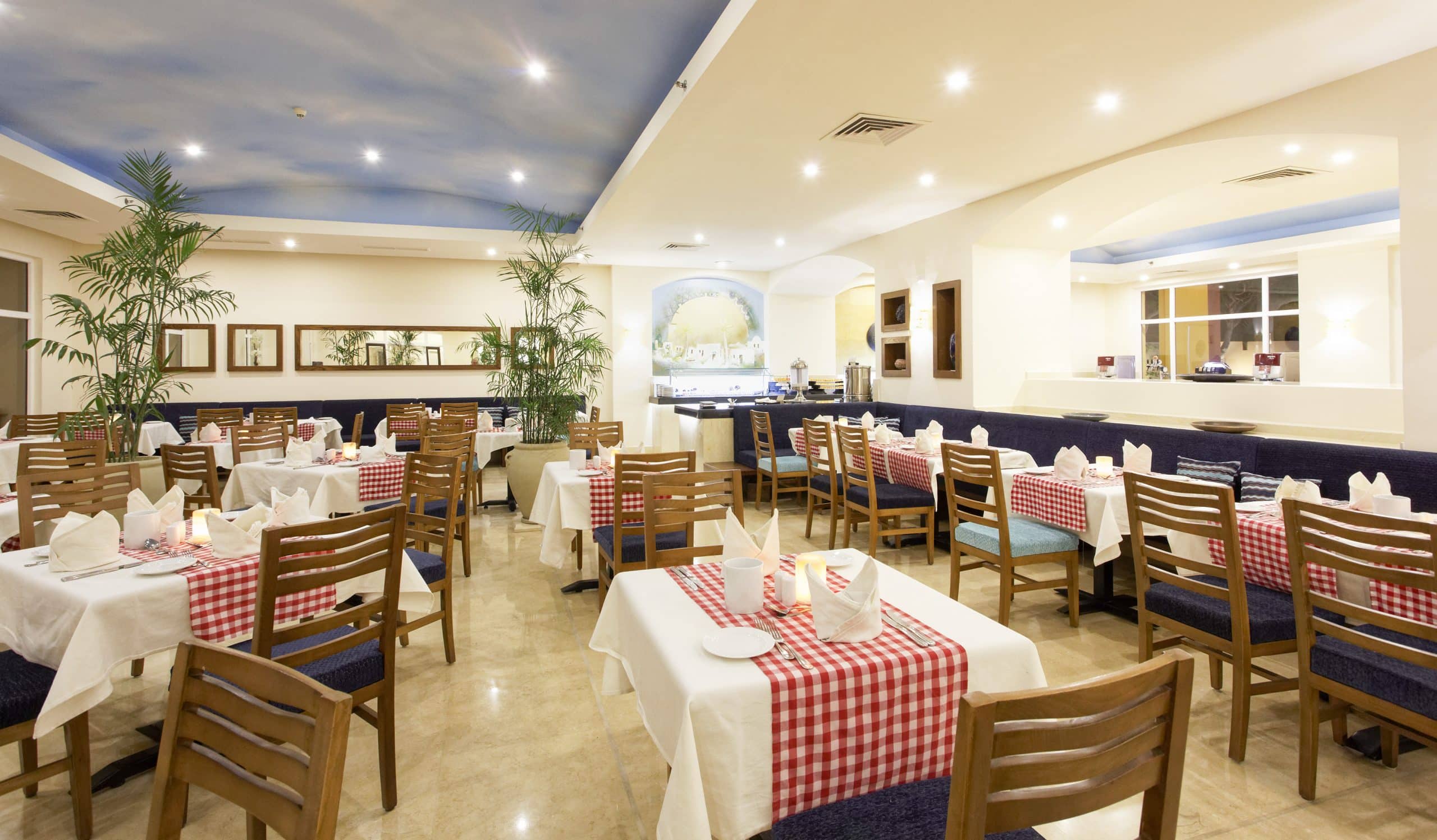 Empty Three Corners restaurant with checkered tablecloths and wooden chairs under a blue ceiling.