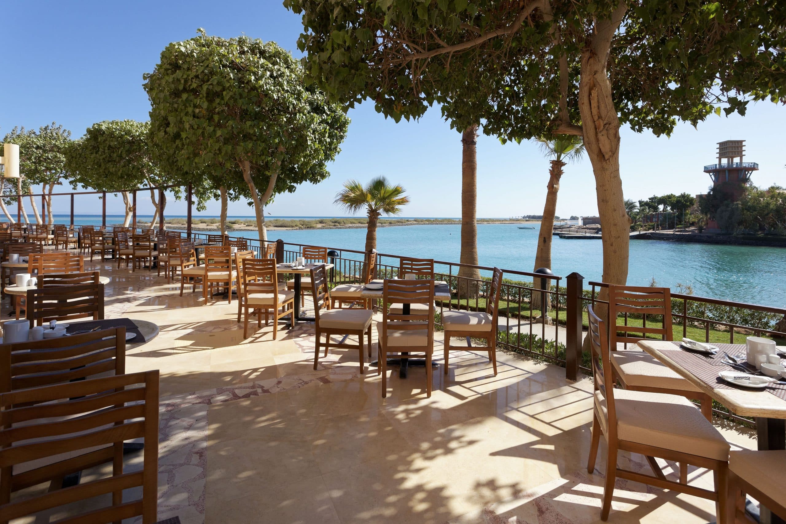 Outdoor dining area at Three Corners Ocean View with wooden tables by a scenic body of water.