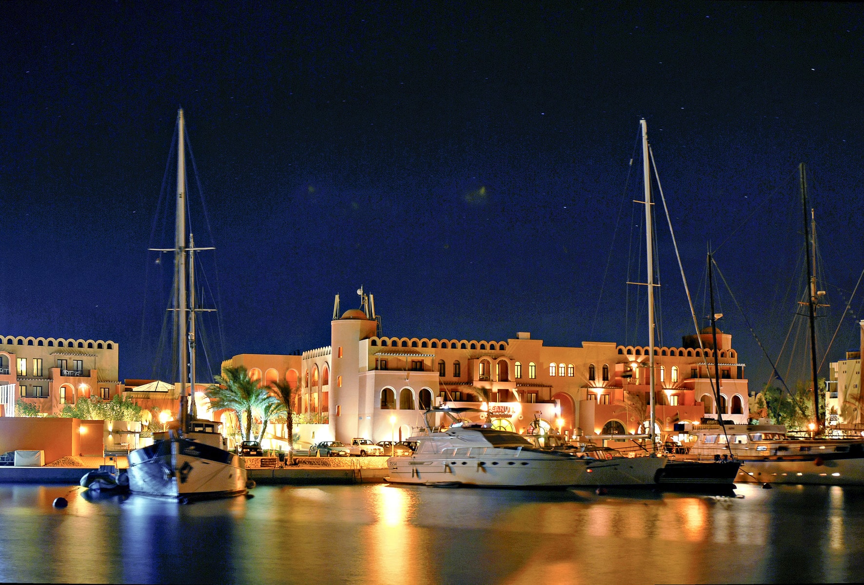 Night view of Three Corners Ocean View marina with yachts and lit buildings under a starry sky.