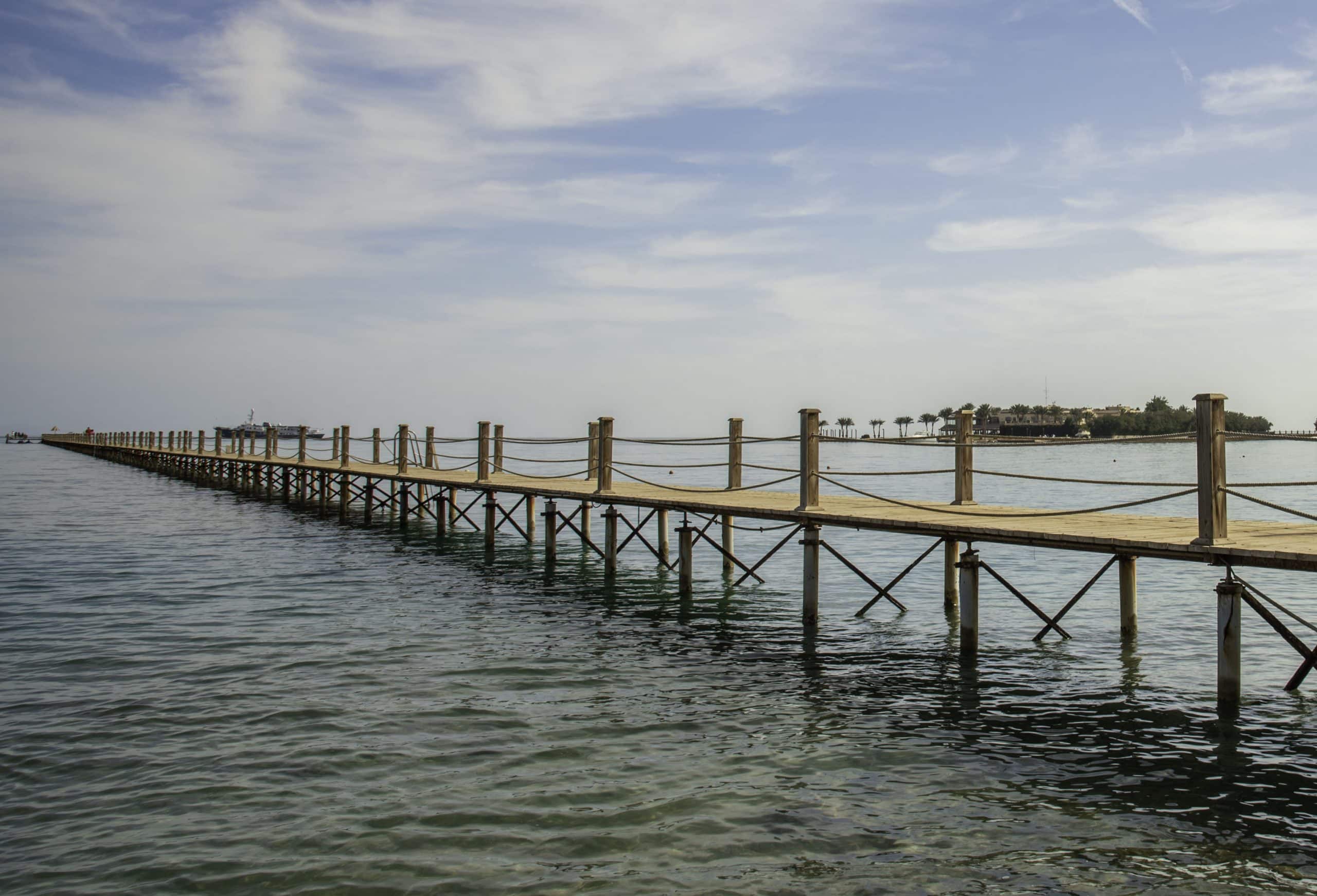 A long wooden pier at Three Corners Ocean View extends into calm water under a cloudy sky.
