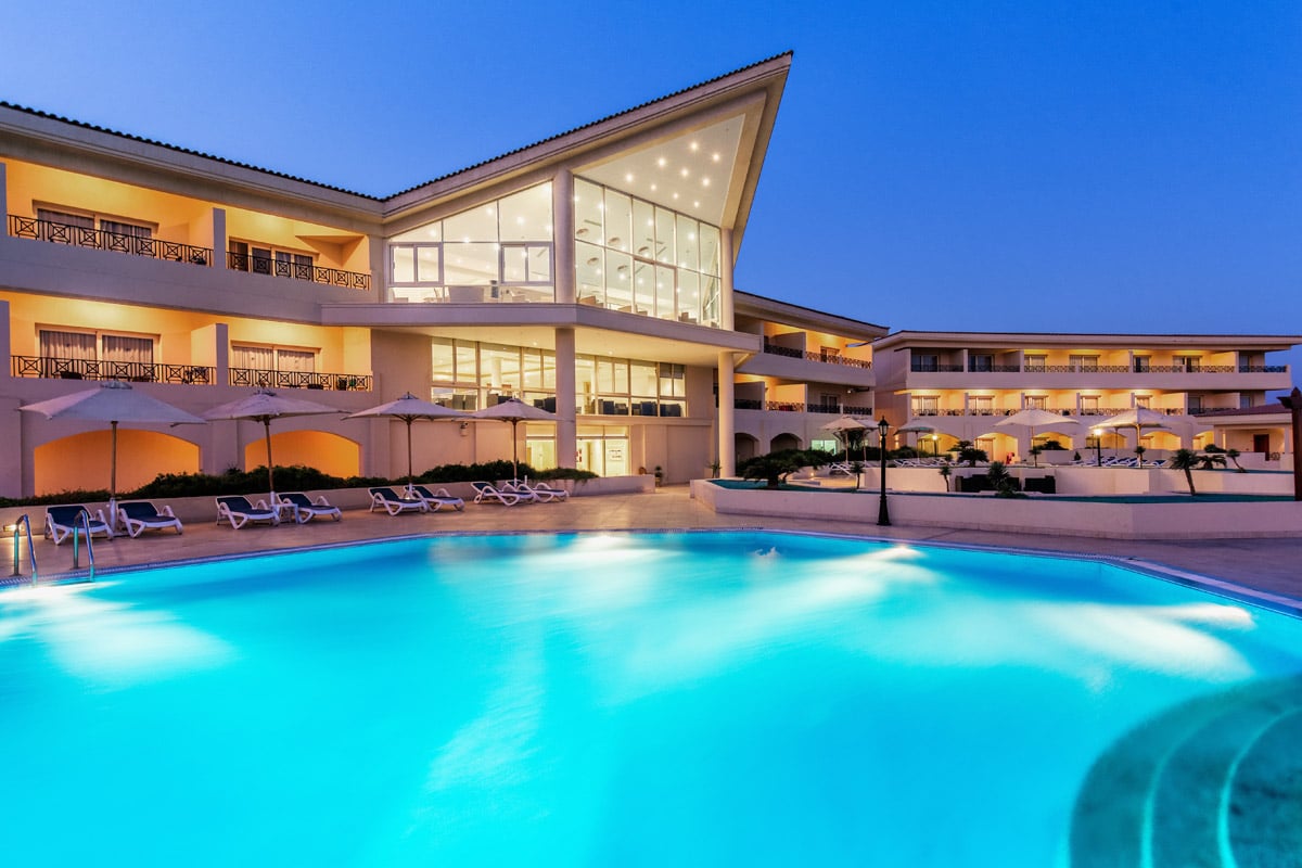 Cleopatra Luxury Resorts modern exterior with a large illuminated pool at dusk.