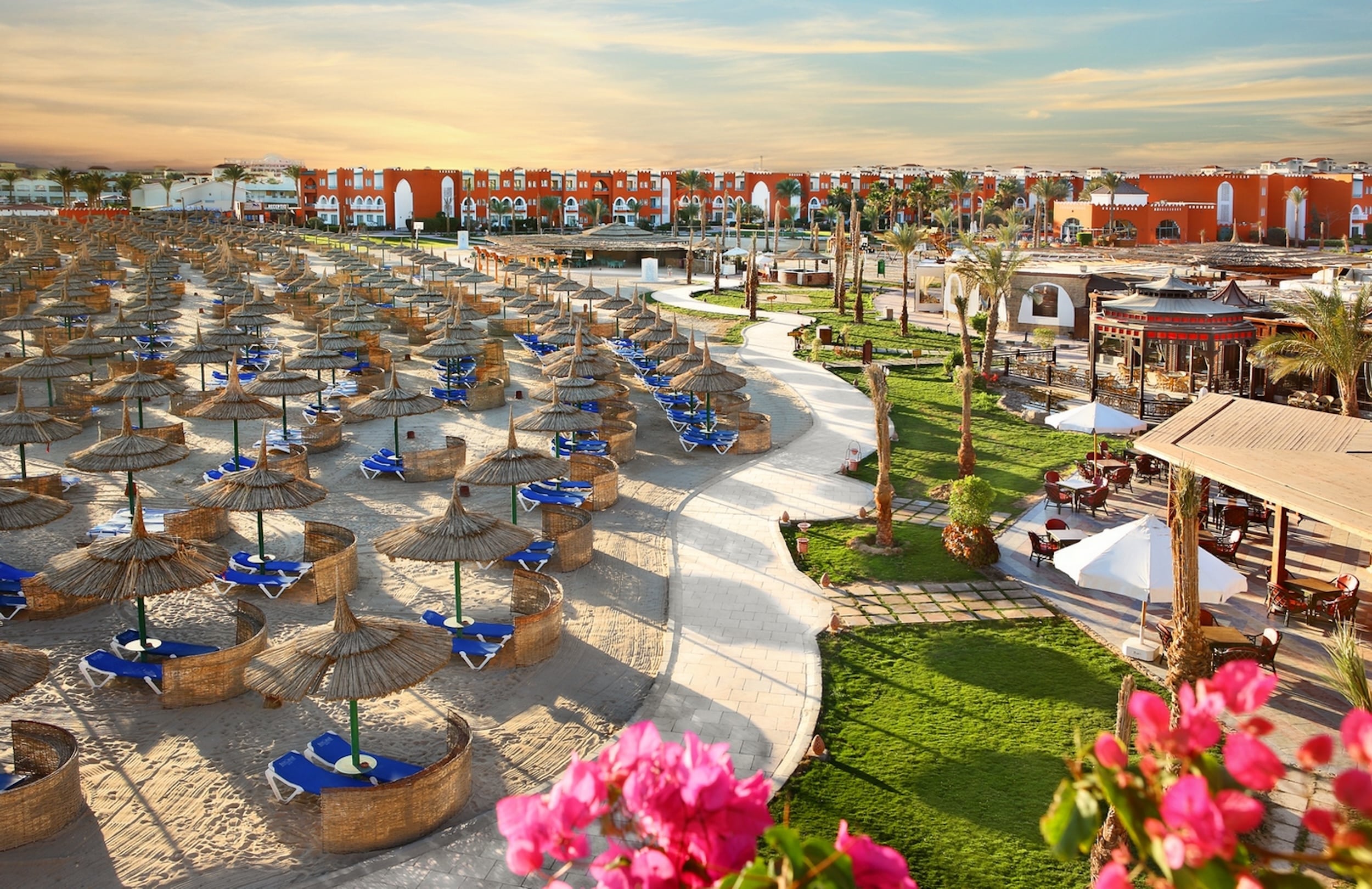 Sunrise Garden Beach resort with straw umbrellas, lounge chairs, green lawns, and vibrant buildings.