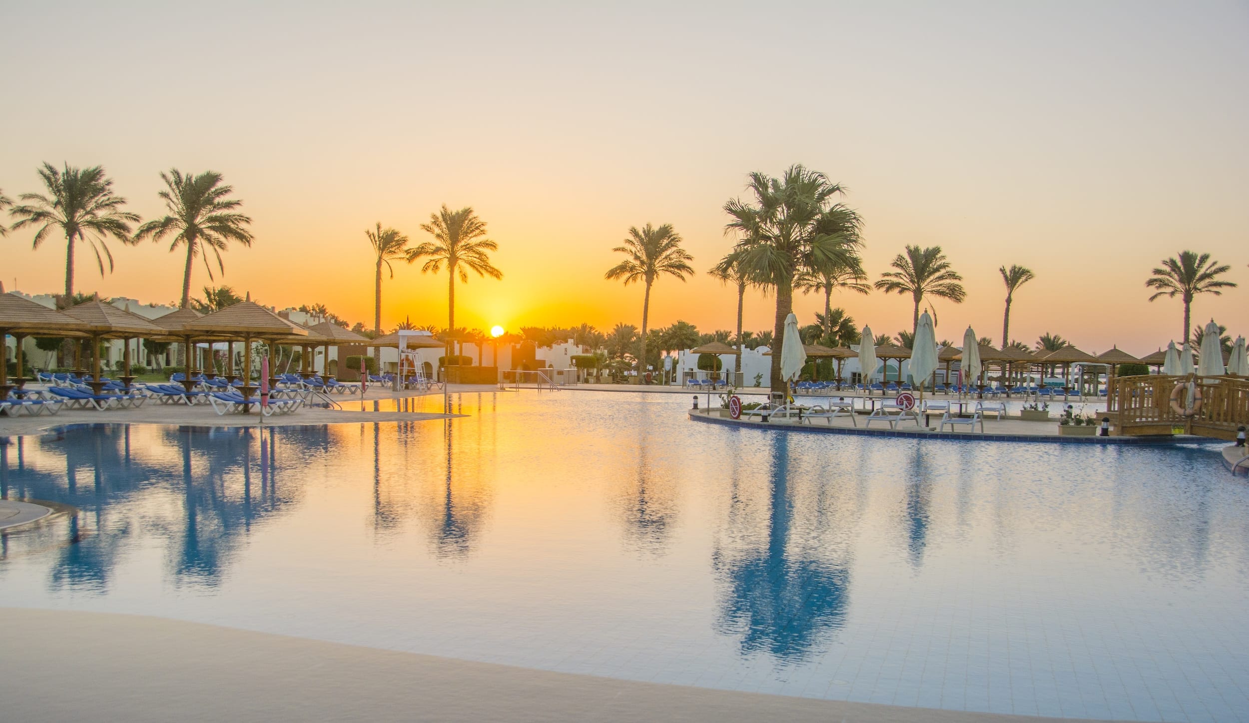 Sunset views at Sunrise Royal Makadi Resort, with lounge chairs and palm trees by the pool.