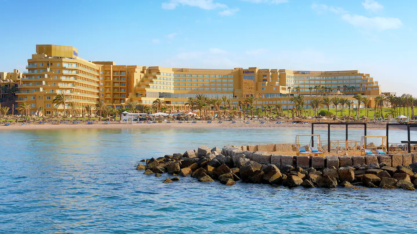 Hilton Hurghada: Beachfront hotel with palm trees and sun loungers by the sea.