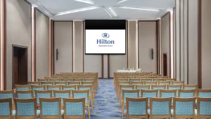 Rows of chairs face a screen displaying the Hilton Hurghada logo in an empty conference room.