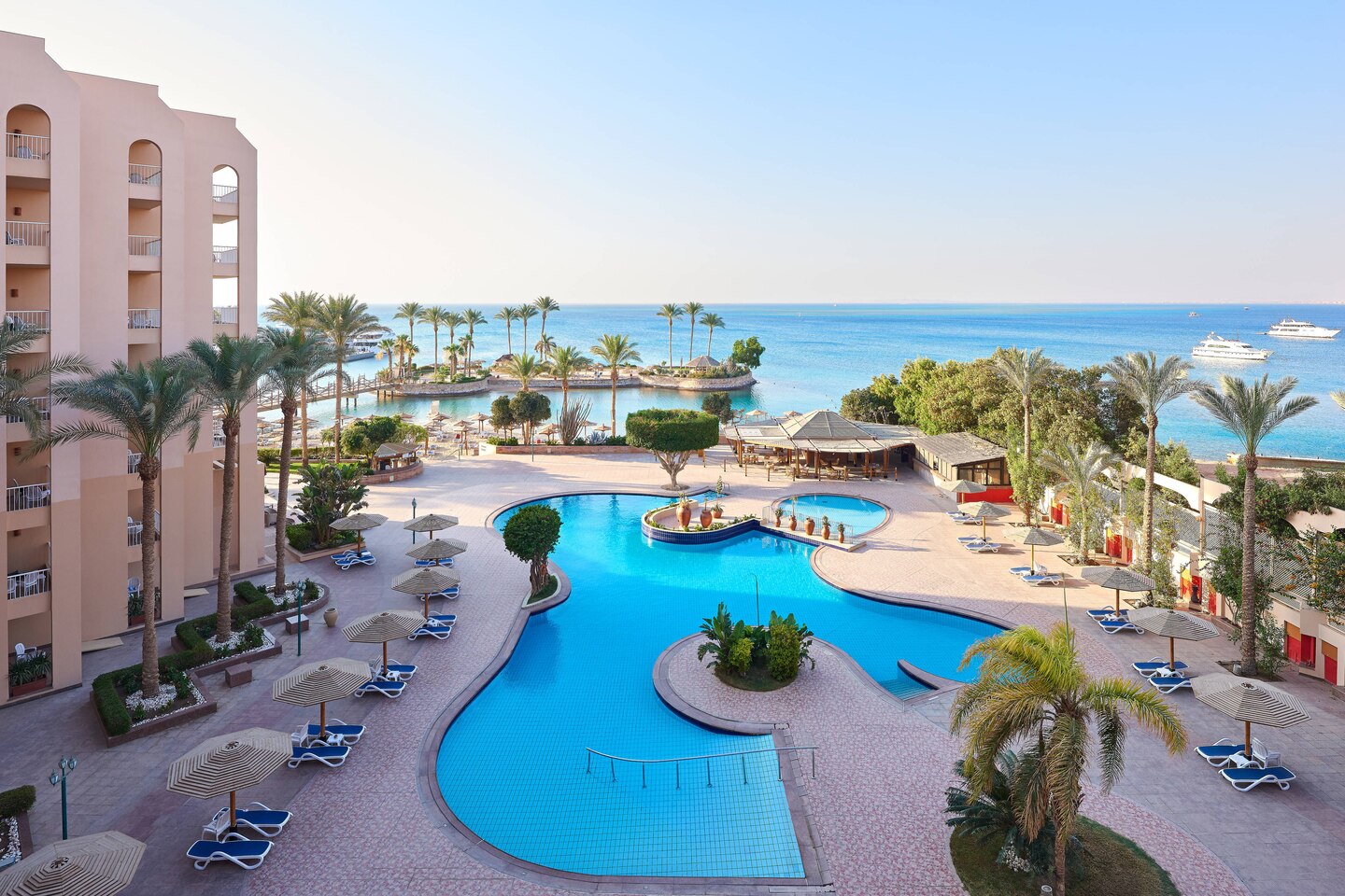 Hurghada Marriott Beach Resort: palm trees, pool, and ocean view with boats in the distance.