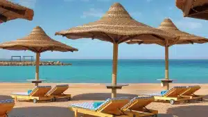 Beach scene at Hilton Hurghada with straw umbrellas, wooden chairs, and clear blue sea.