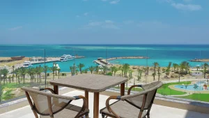 Outdoor table and chairs at Hilton Hurghada marina, with boats and palm trees by the turquoise sea.