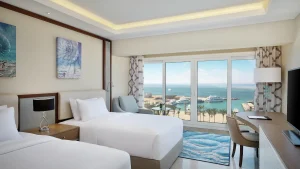 Twin-bed room at Hilton Hurghada with desk and ocean view through a large window.