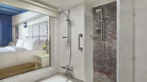 Modern Hilton Hurghada bathroom with tub, handheld shower, and frosted window view.