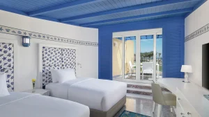 Hilton Hurghada room: two beds, blue accents, and a balcony view with lush greenery.