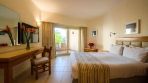Hotel room with a bed, desk, chair, and balcony overlooking Fort Arabesque Resort greenery.