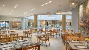 Modern restaurant at Hilton Hurghada with wooden furniture, marble tables, and large paintings.