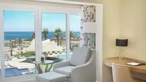 Hilton Hurghada room with armchair and desk, overlooks pool and beach through large windows.