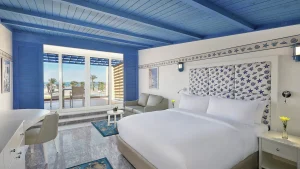 Hilton Hurghada hotel room with a double bed, glass doors, and a balcony view of palm trees and sea.