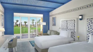 Hilton Hurghada room: two beds, a sofa, and terrace view of a garden with palm trees.