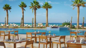 Hilton Hurghadas outdoor dining area by a pool with palm trees and lounge chairs.