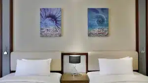 Two beds, white pillows at Hilton Hurghada, black lamp, and abstract artworks on the wall.