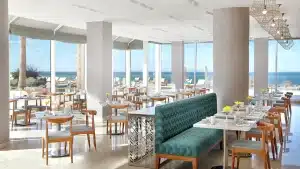 Bright Hilton Hurghada restaurant with ocean view, wooden chairs, and teal cushioned seating.