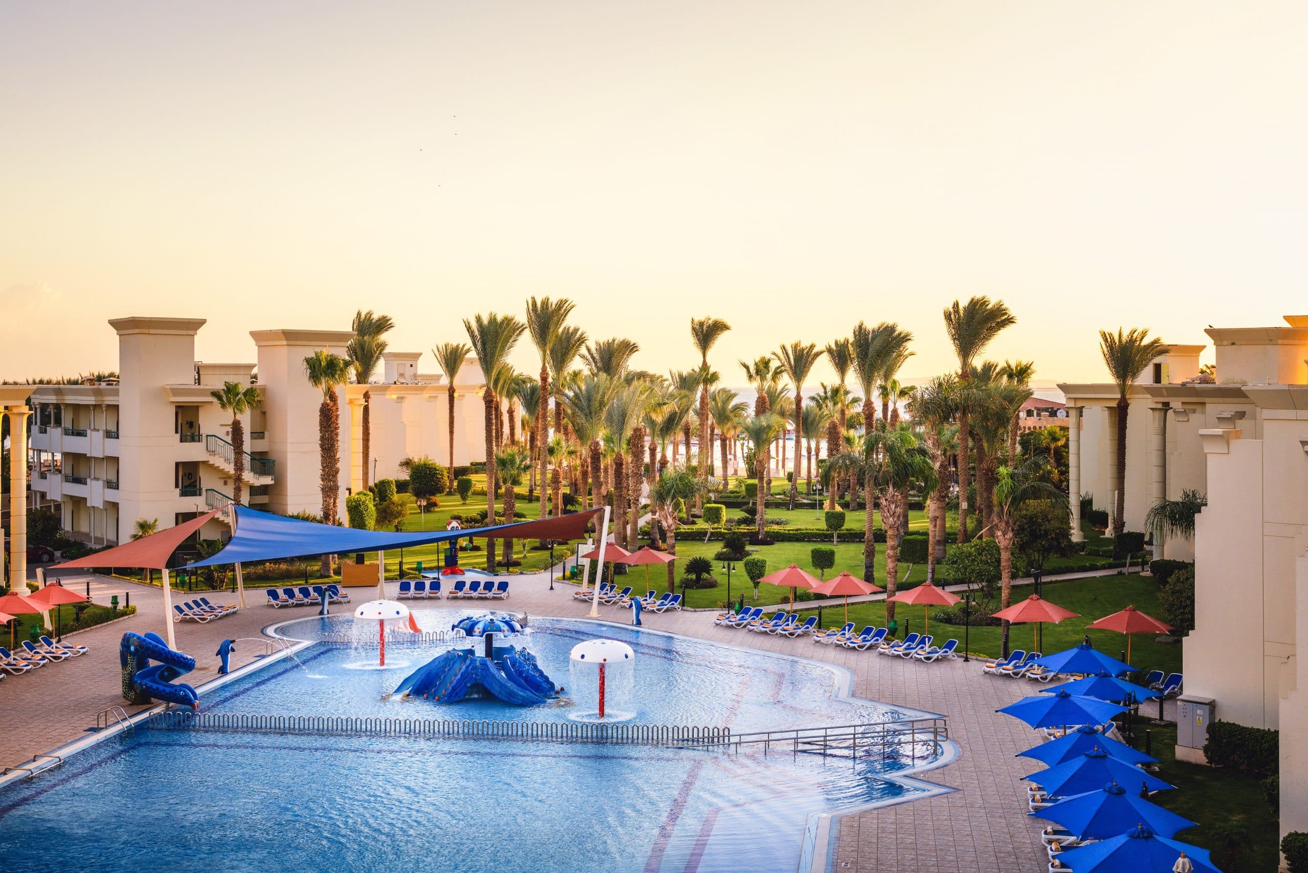 Swiss Inn Resort Hurghada pool, with palm trees, lounge chairs, and sunshades at sunset.