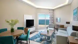 Modern Hilton Hurghada living room with ocean view, sofa, TV, and round table with blue chairs.
