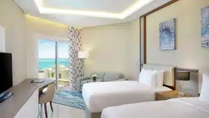 Hilton Hurghada room with two beds, sofa, ocean-view balcony, and modern decor.
