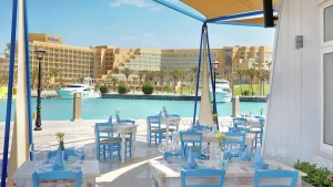 Outdoor dining area overlooking a marina with boats and Hilton Hurghada in the background.