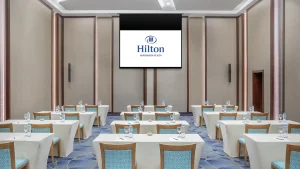 Hilton Hurghada room with tables, chairs, and a projector screen showing the Hilton logo.