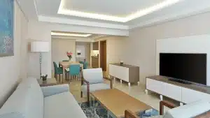 Modern living room at Hilton Hurghada, with beige furniture, dining table, and wall TV.