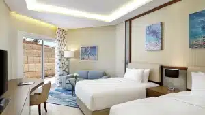 Hilton Hurghada room with two beds, sofa, desk, and a window overlooking the outdoor area.