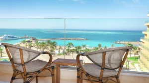 Two wicker chairs on a Hilton Hurghada balcony overlook a turquoise sea and marina.