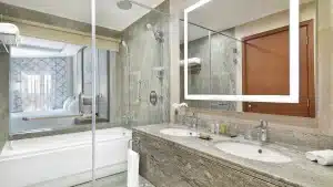 Modern Hilton Hurghada bathroom with double sink, backlit mirror, bathtub, and glass shower.
